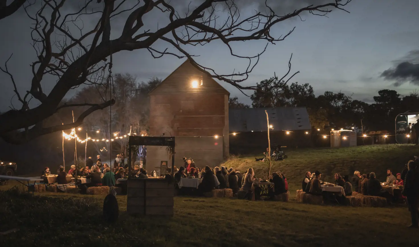 Guests at long tables under string lights at ECHO East Coast Harvest Odyssey festival at dusk, Cranbrook, Tasmania