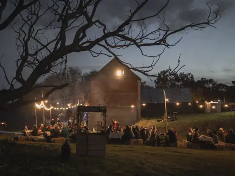 Guests at long tables under string lights at ECHO East Coast Harvest Odyssey festival at dusk, Cranbrook, Tasmania