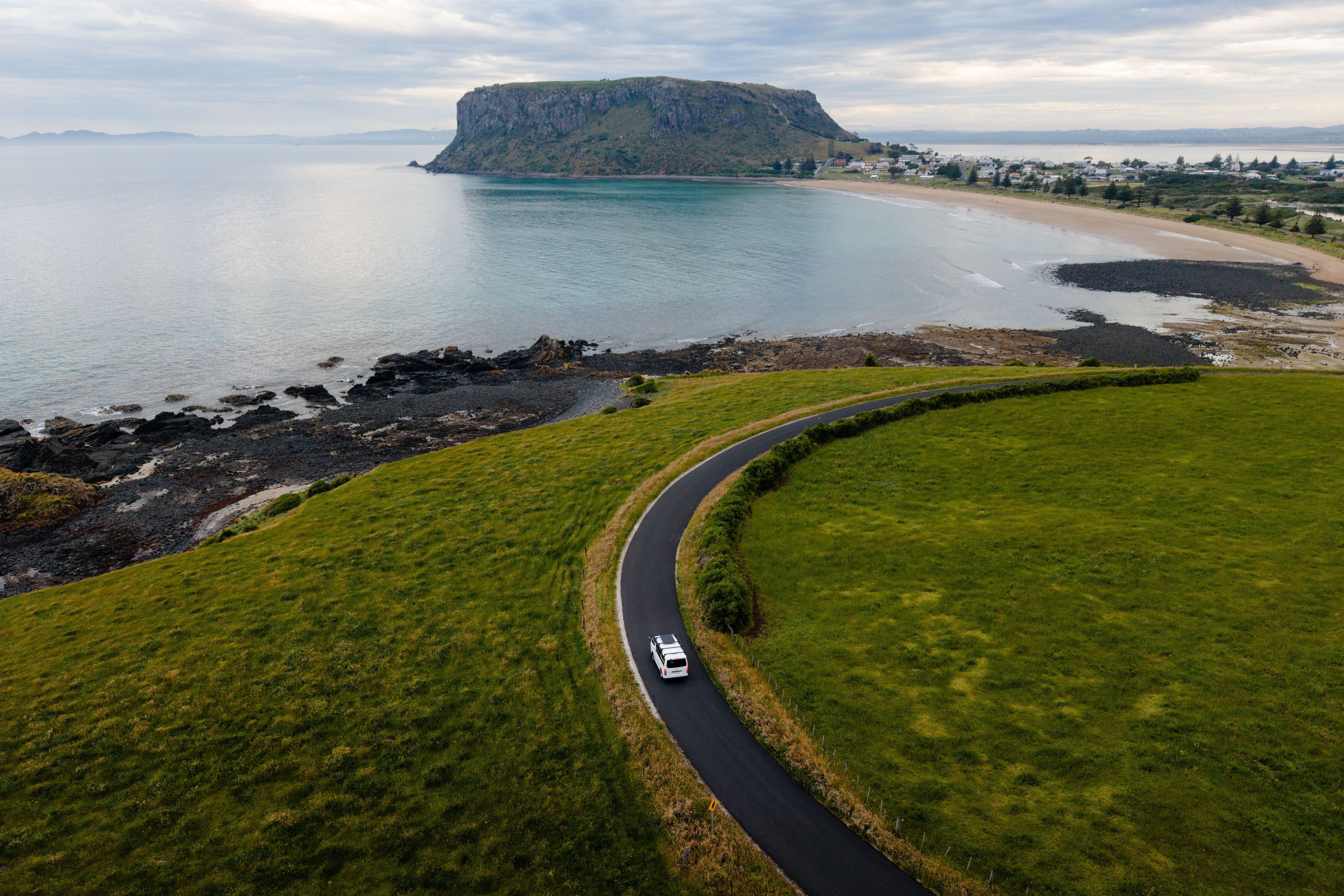 Aerial view of a vehicle on a coastal road approaching The Nut at Stanley, Tasmania
