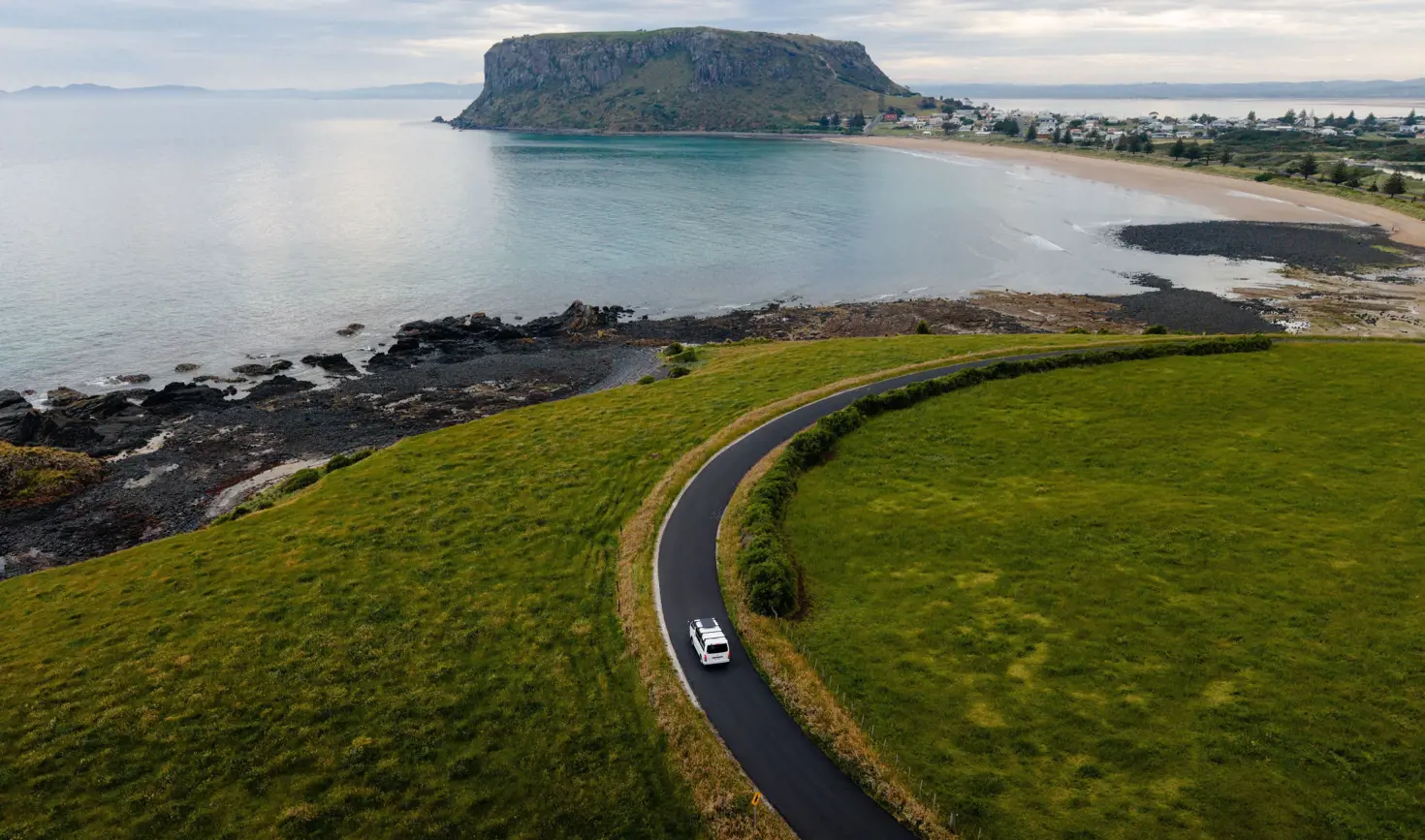 Aerial view of a vehicle on a coastal road approaching The Nut at Stanley, Tasmania