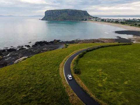 Aerial view of a vehicle on a coastal road approaching The Nut at Stanley, Tasmania
