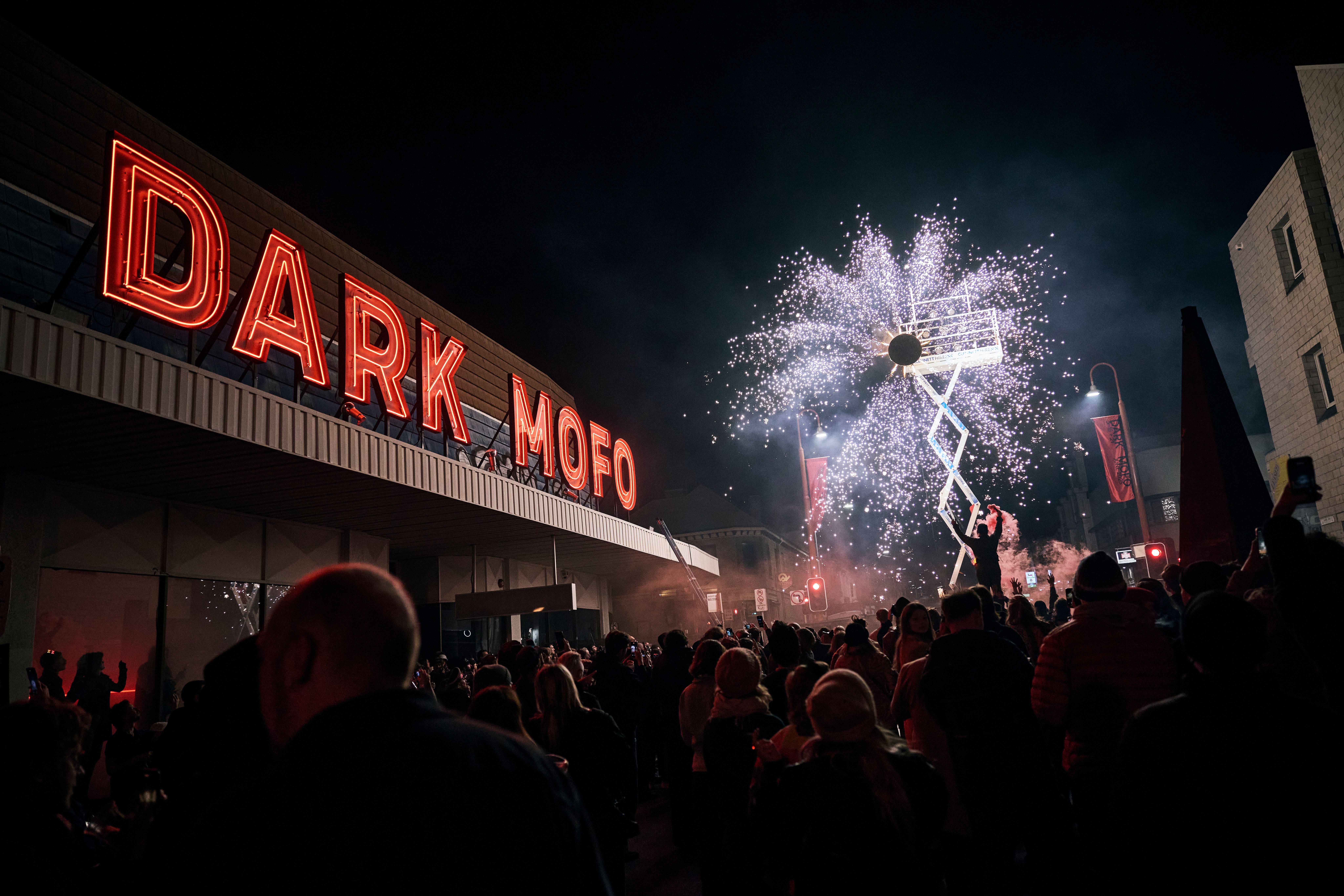 A crowd watching pyrotechnics under the red Dark Mofo neon sign at Night Mass: God Complex during Dark Mofo, Hobart, Tasmania