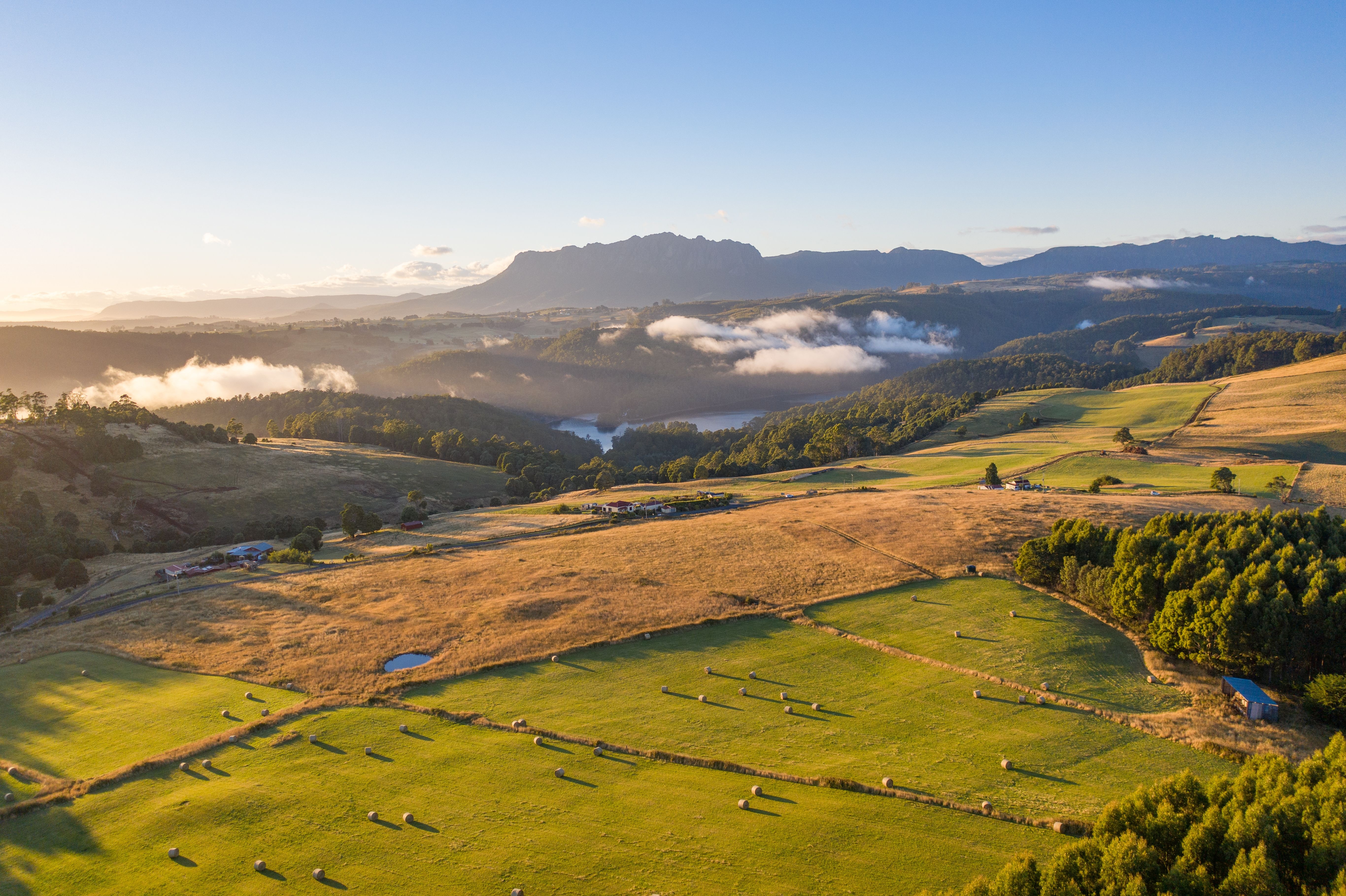 Aerial view of farmland with hay bales and Mount Roland in the background at golden hour, Wilmot, Tasmania