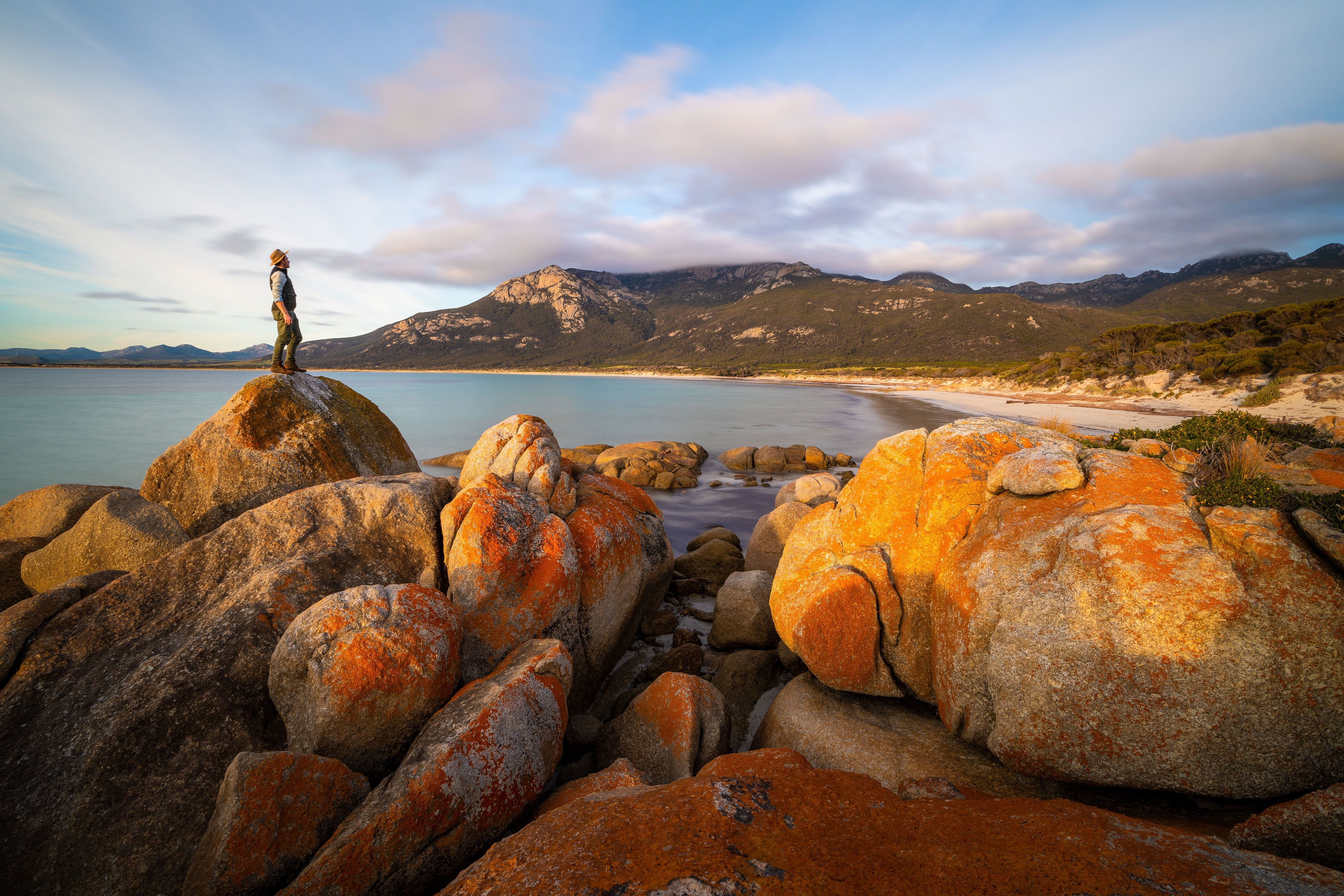 A walker on a lichen covered granite boulder overlooking Fotheringate Bay, Strzelecki National Park, Flinders Island, Tasmania