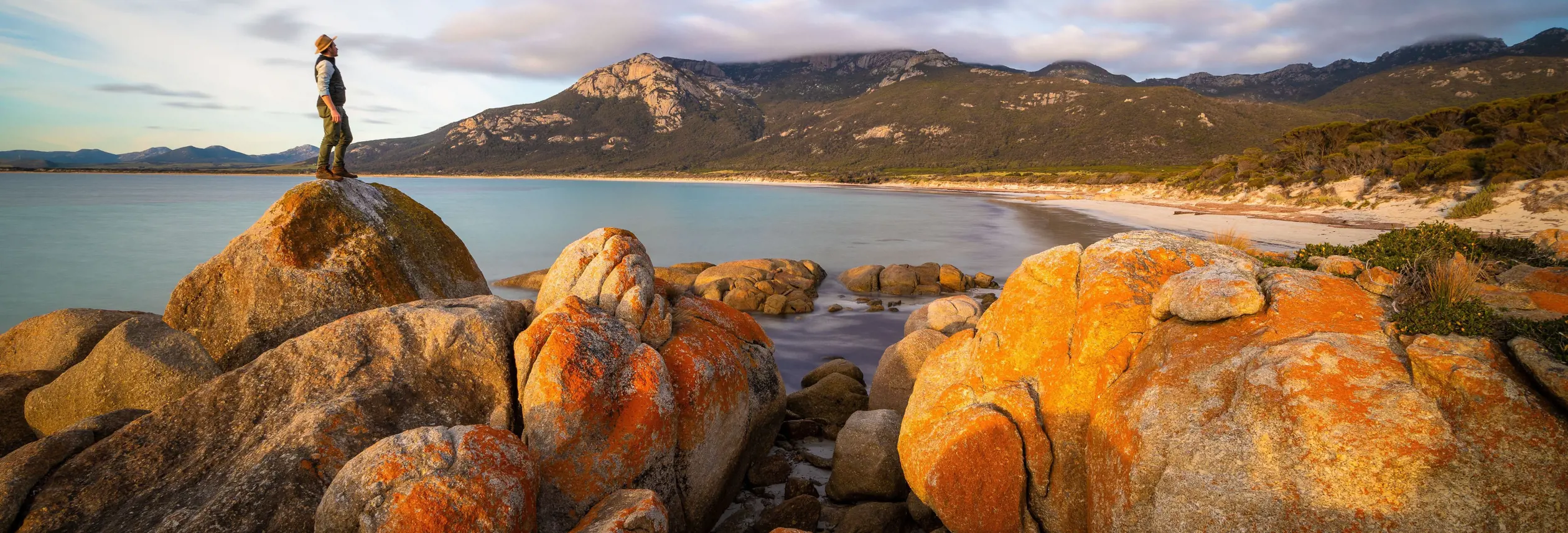 A walker on a lichen covered granite boulder overlooking Fotheringate Bay, Strzelecki National Park, Flinders Island, Tasmania