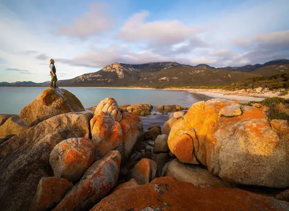A walker on a lichen covered granite boulder overlooking Fotheringate Bay, Strzelecki National Park, Flinders Island, Tasmania