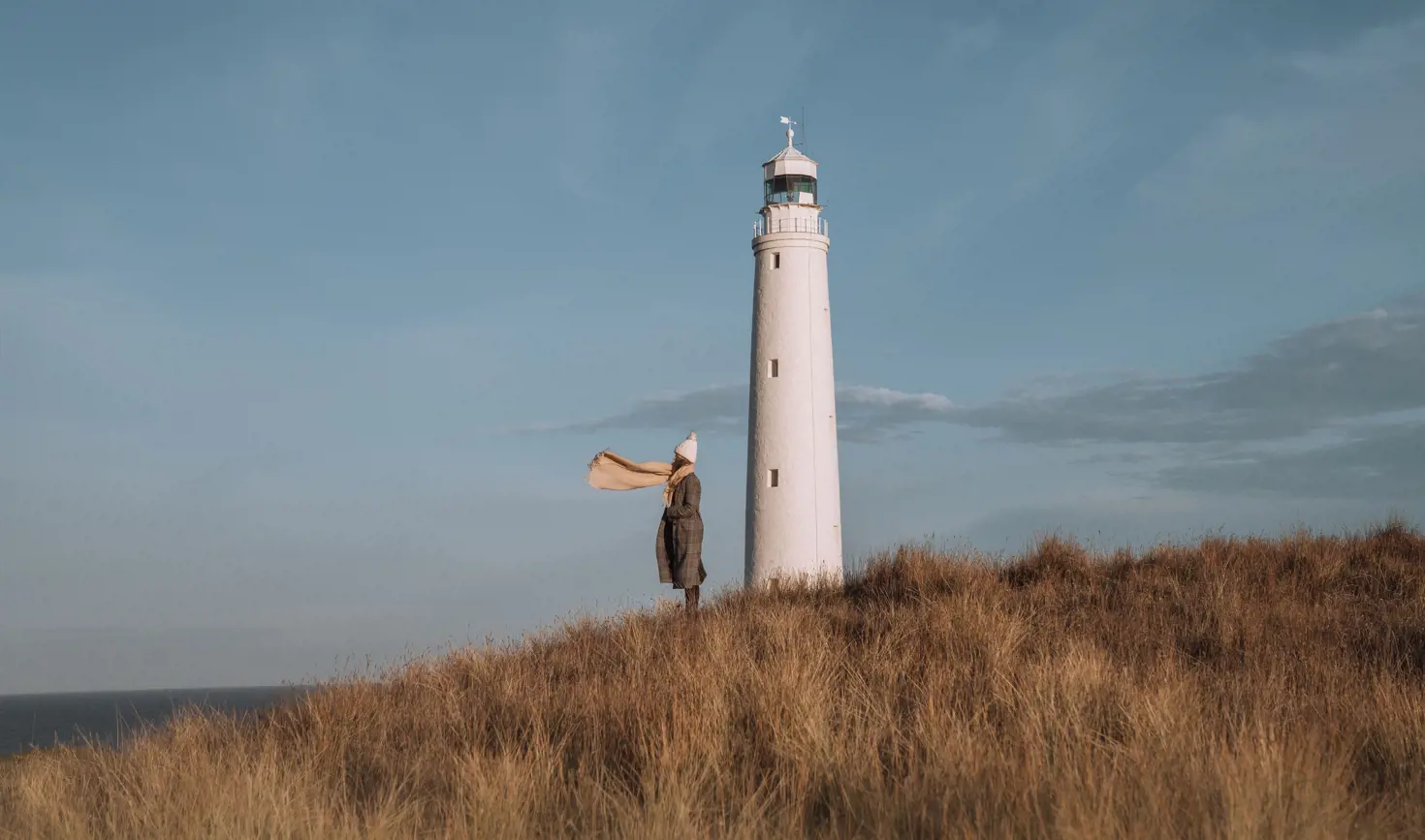 A person with a scarf blowing in the wind standing beside Cape Wickham Lighthouse, King Island, Tasmania
