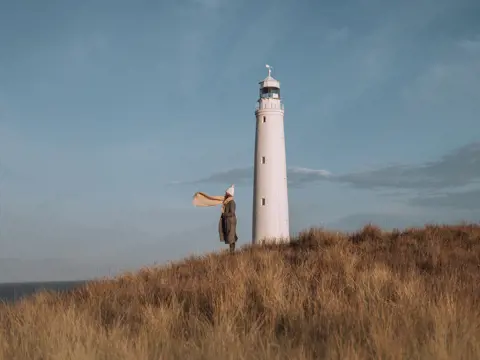 A person with a scarf blowing in the wind standing beside Cape Wickham Lighthouse, King Island, Tasmania