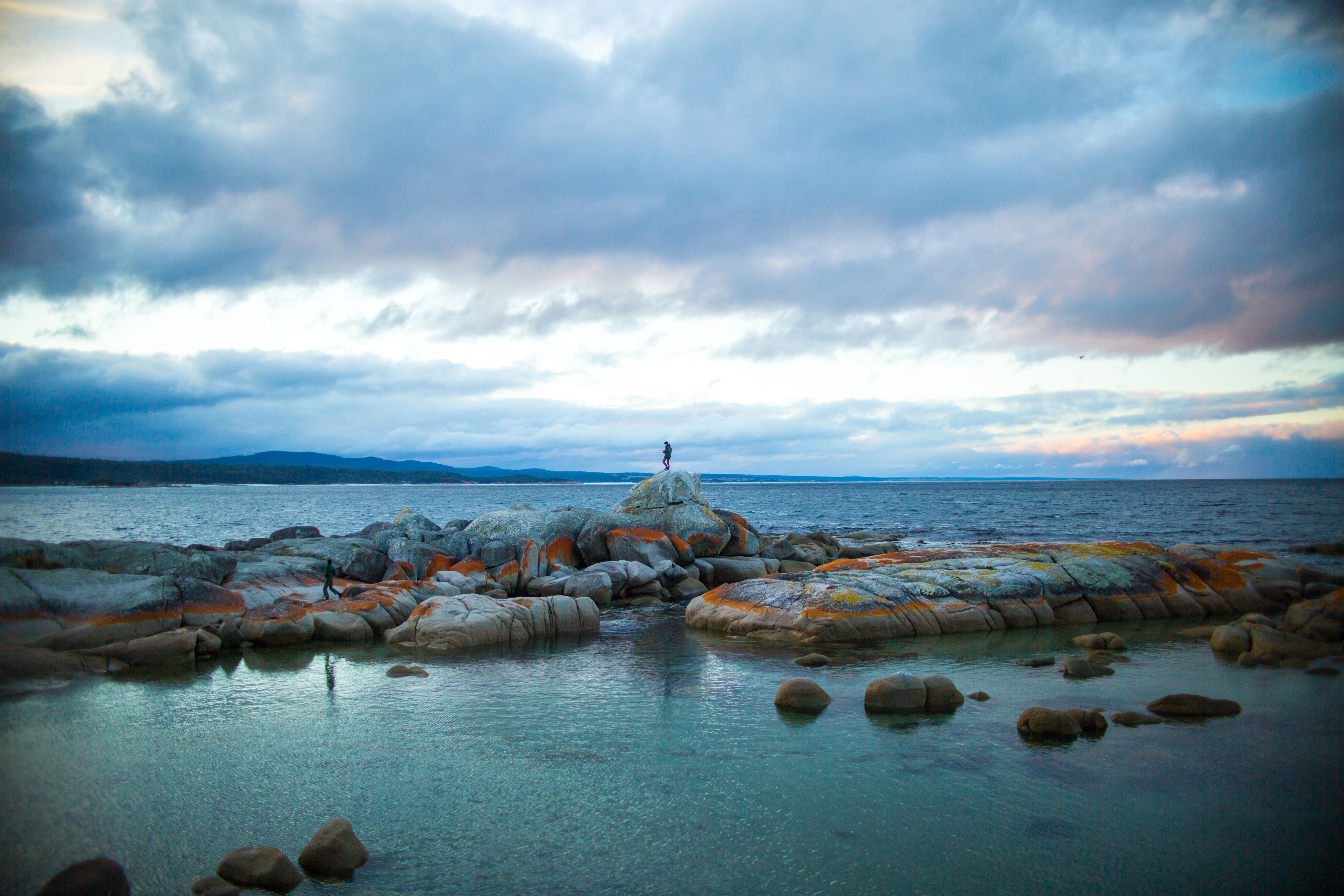 A person standing on lichen covered granite boulders at The Gulch, Binalong Bay, larapuna / Bay of Fires area