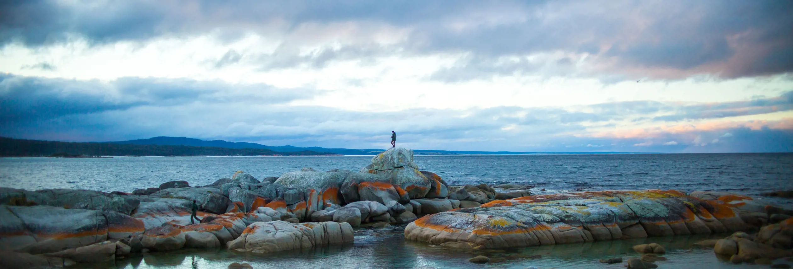 A person standing on lichen covered granite boulders at The Gulch, Binalong Bay, larapuna / Bay of Fires area