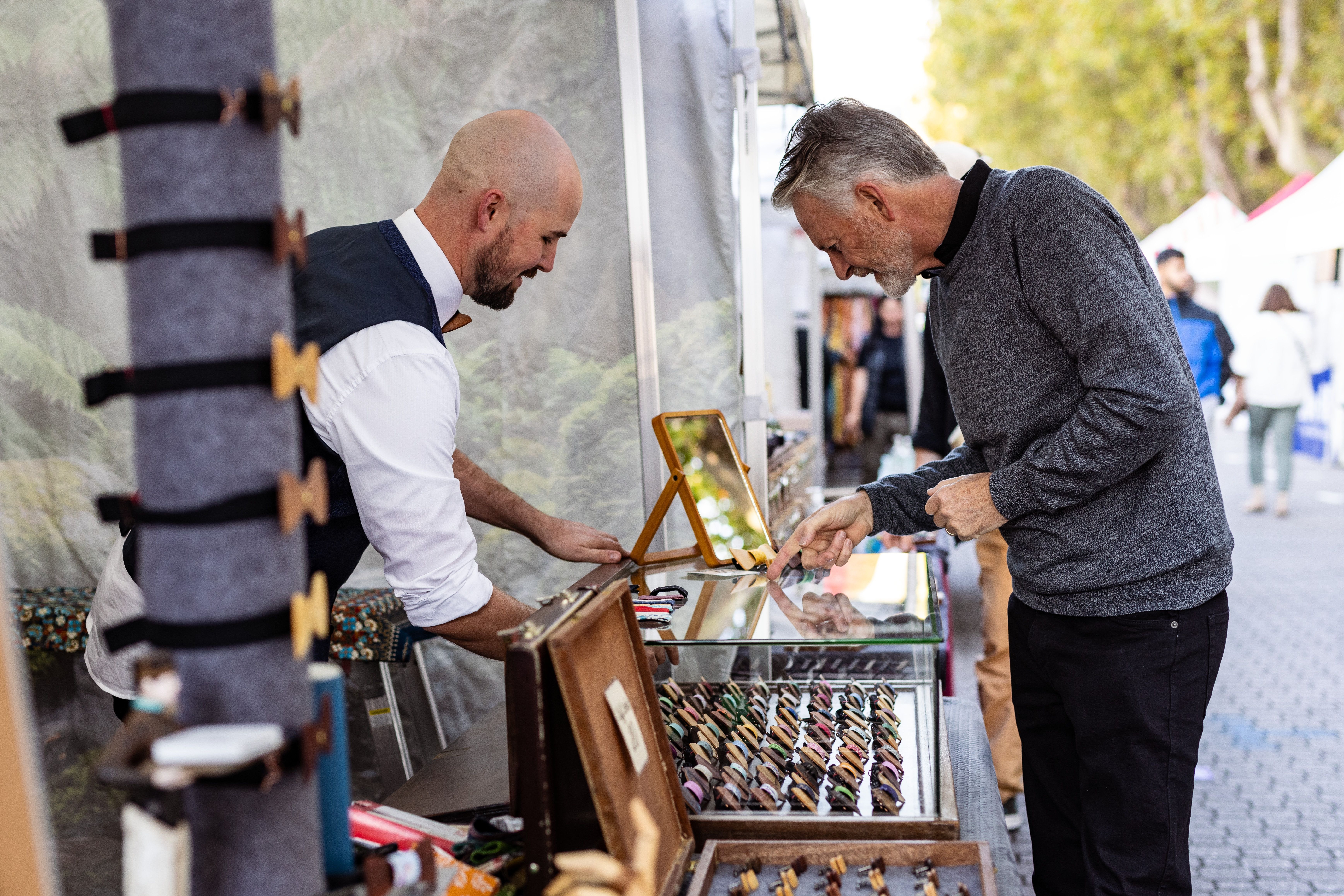 A stallholder showing a customer accessories at a Salamanca Market stall, Salamanca Place, Hobart