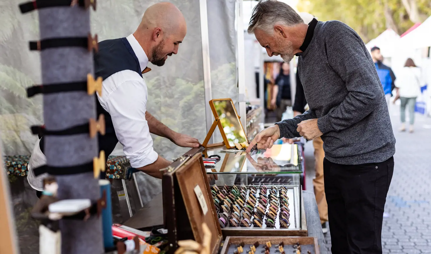 A stallholder showing a customer accessories at a Salamanca Market stall, Salamanca Place, Hobart