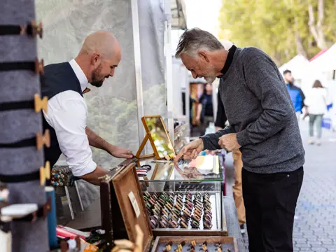 A stallholder showing a customer accessories at a Salamanca Market stall, Salamanca Place, Hobart