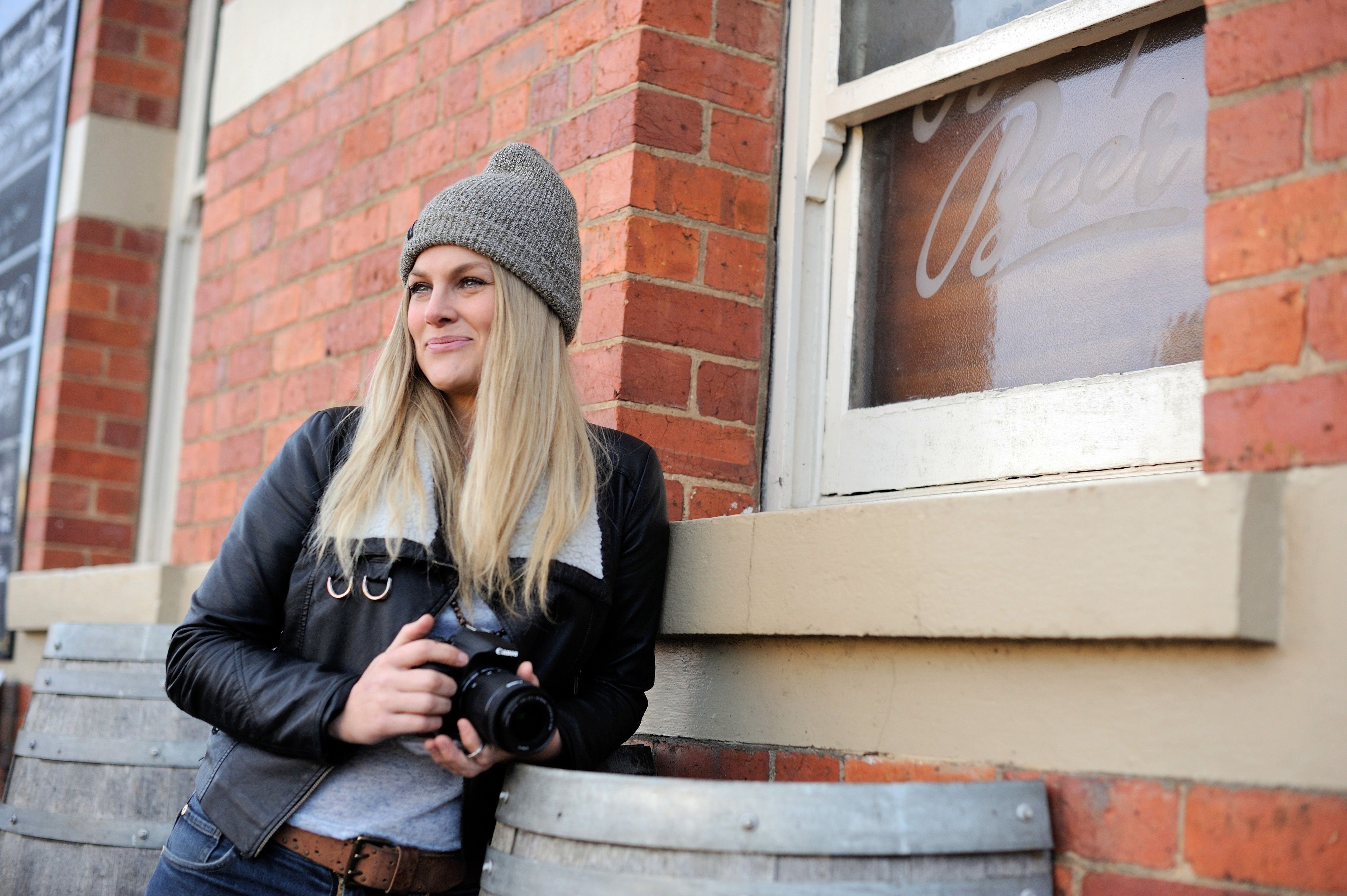 A photographer with a camera leaning against the brick wall of the Empire Hotel, Deloraine