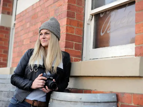 A photographer with a camera leaning against the brick wall of the Empire Hotel, Deloraine