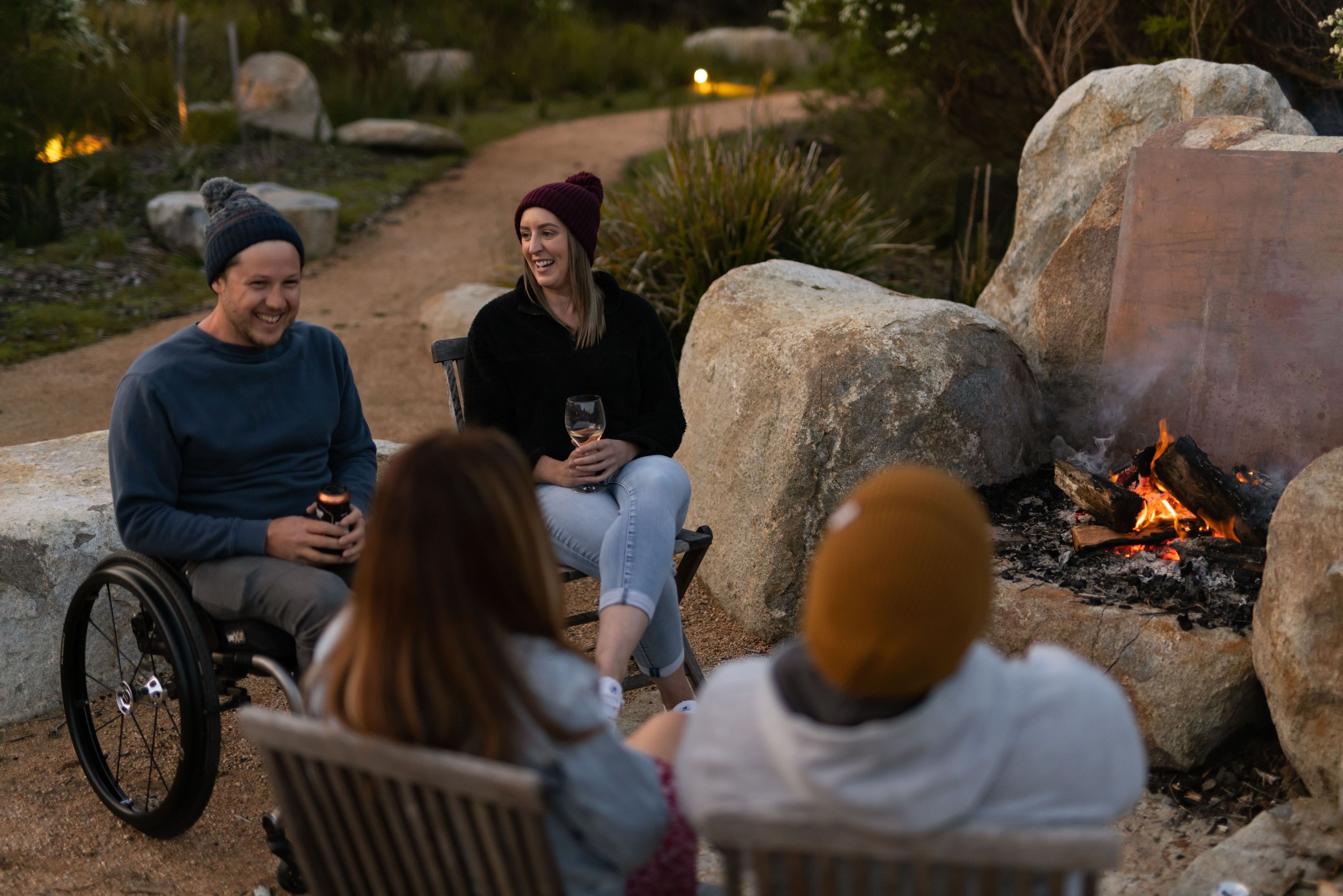Four friends gathered around an open firepit at dusk at Little Beach Co Resort, Chain of Lagoons