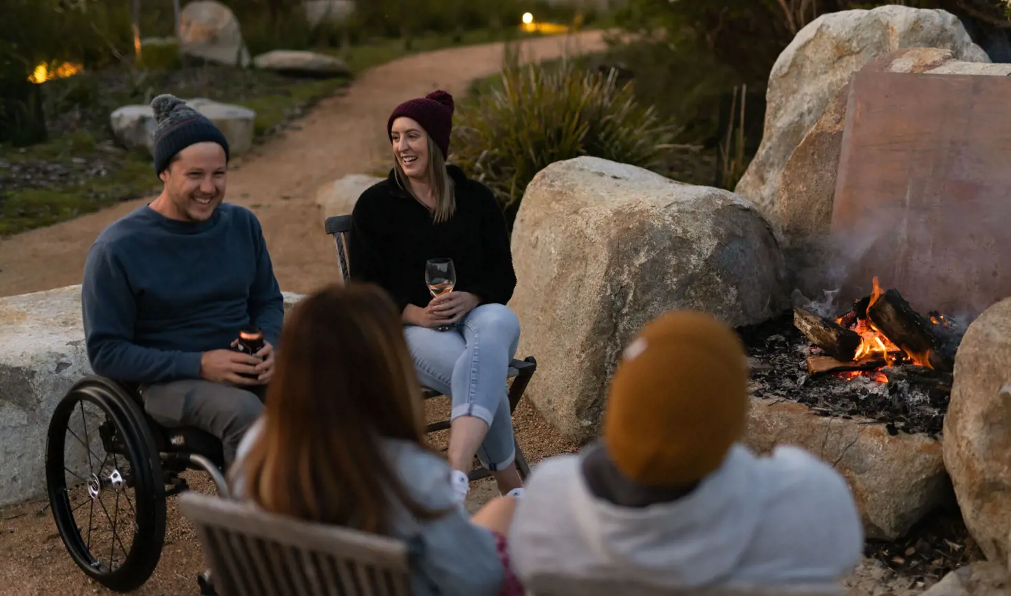 Four friends gathered around an open firepit at dusk at Little Beach Co Resort, Chain of Lagoons