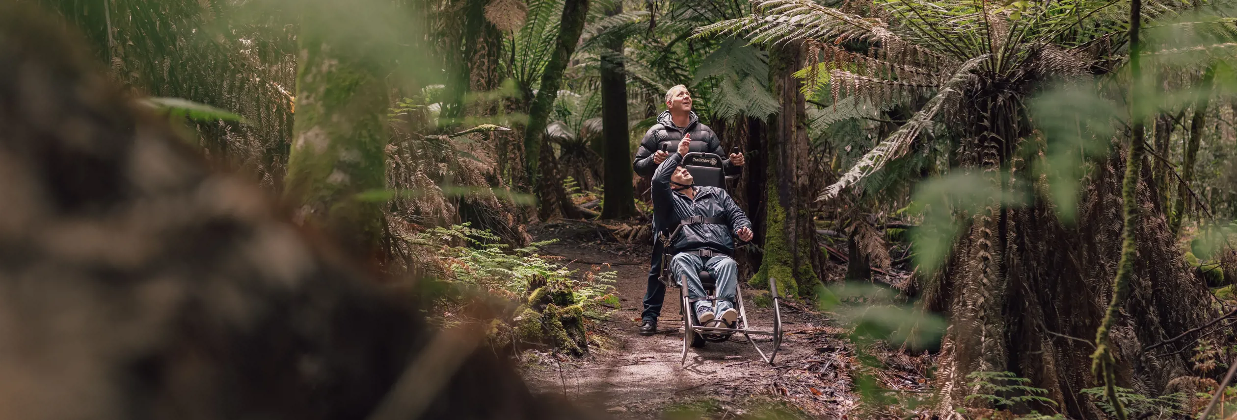A visitor using a TrailRider all-terrain wheelchair with a companion on the Tall Trees Walk, Mount Field National Park