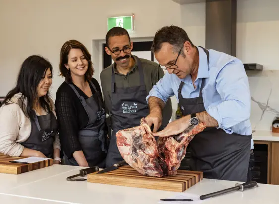 A chef demonstrating butchery to three students in aprons at The Agrarian Kitchen cooking class, New Norfolk