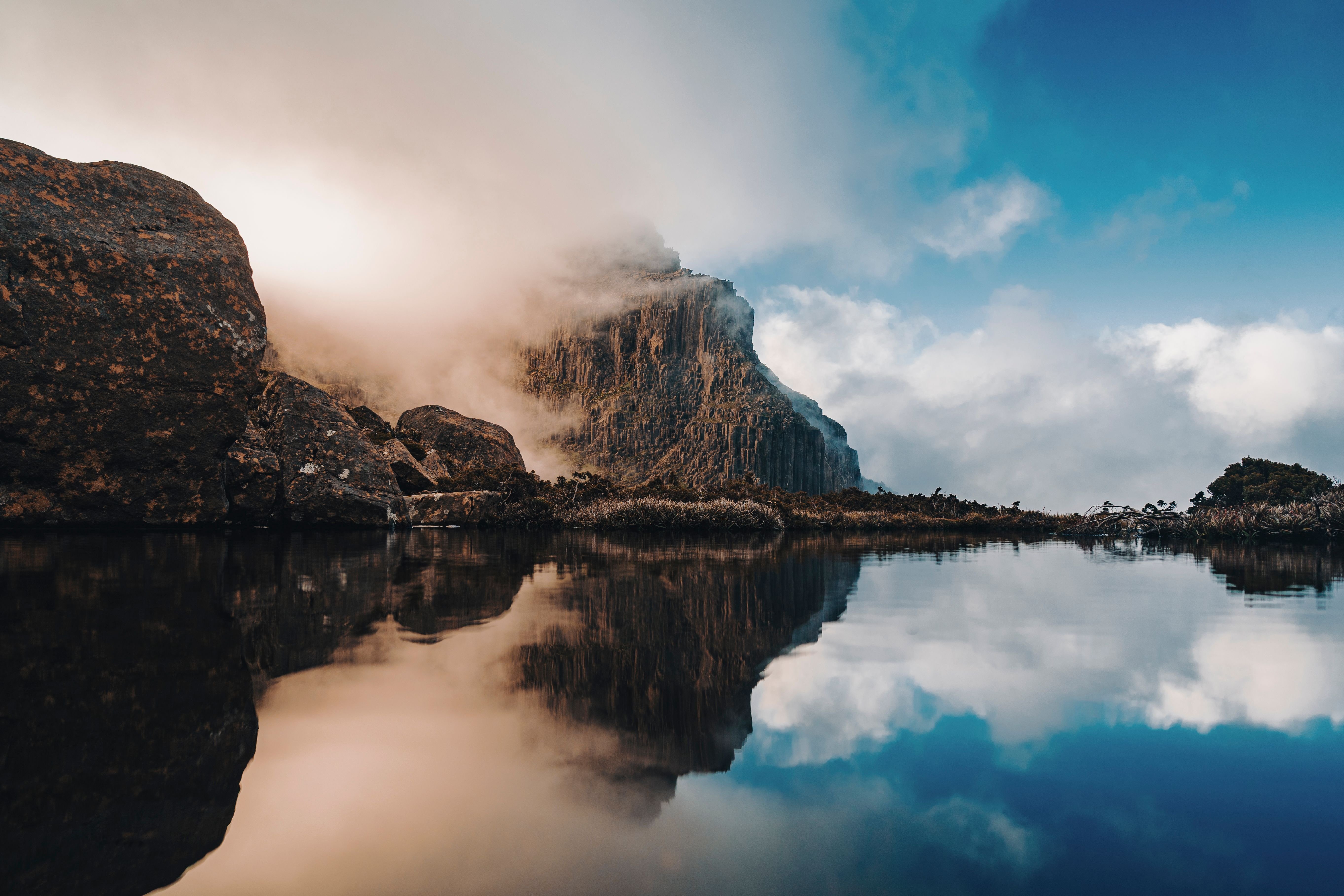 Mist drifting across cliffs on the Mount Anne Circuit reflected in still water, Southwest National Park