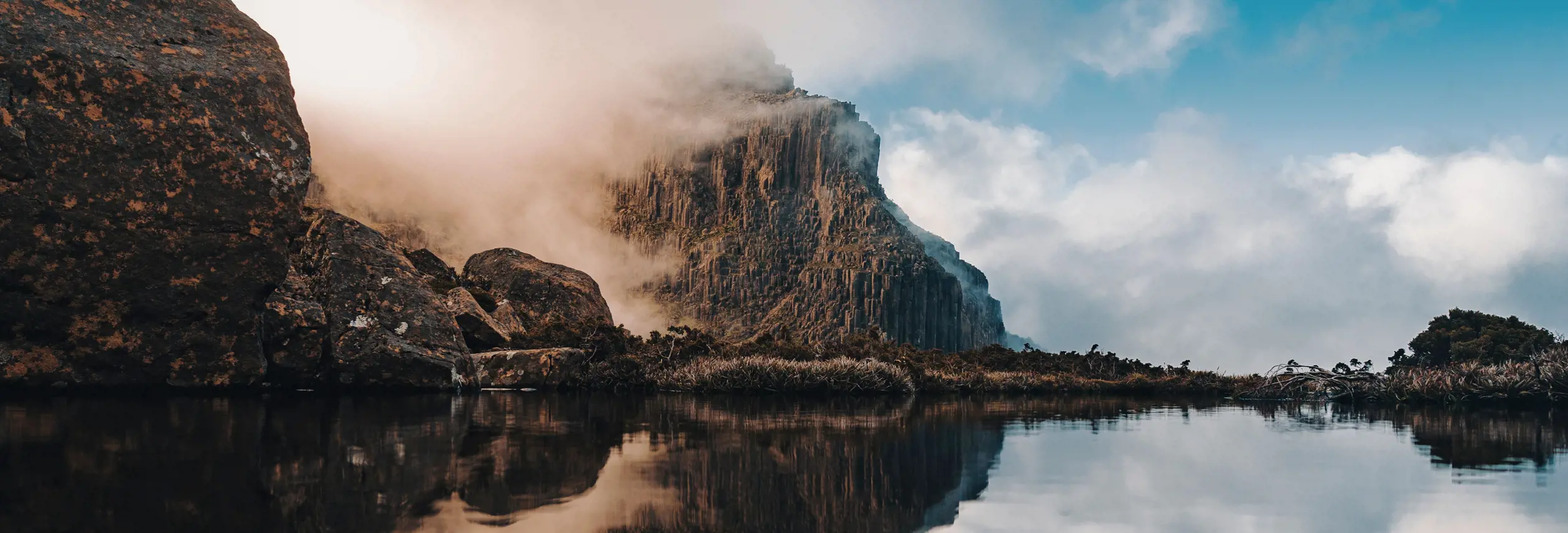 Mist drifting across cliffs on the Mount Anne Circuit reflected in still water, Southwest National Park