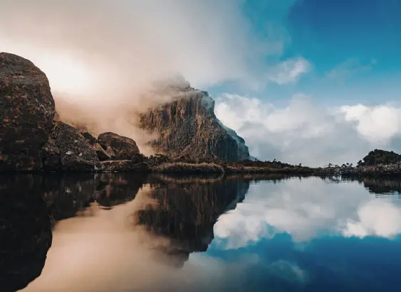 Mist drifting across cliffs on the Mount Anne Circuit reflected in still water, Southwest National Park
