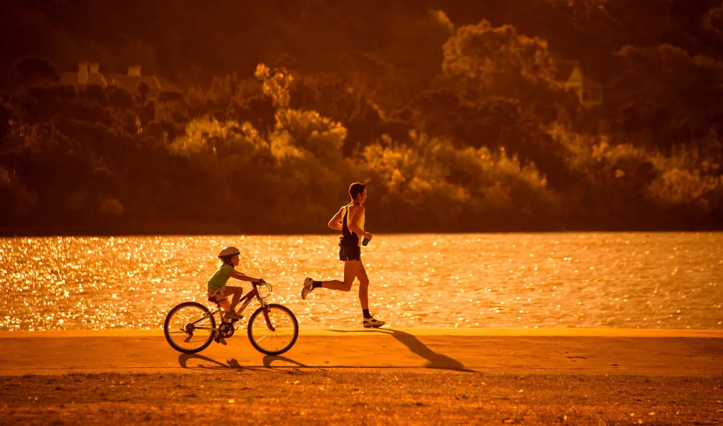 A runner and a child cycling beside the North Esk River at golden hour, Launceston