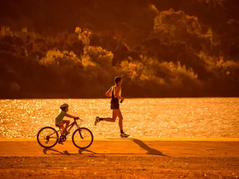 A runner and a child cycling beside the North Esk River at golden hour, Launceston