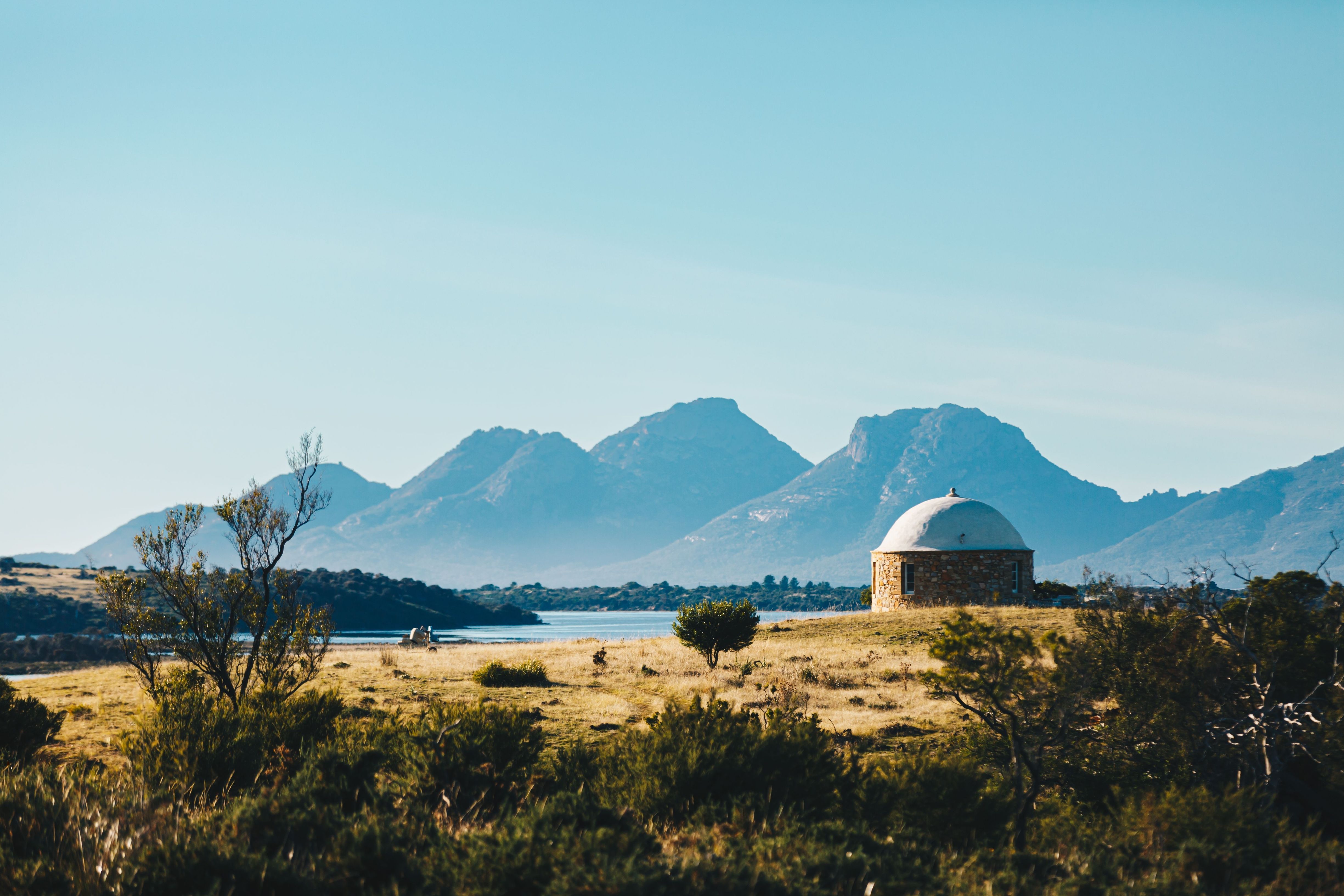 A round stone building with a domed roof in open grassland with water and mountains beyond at The Bend Vineyard, Swansea