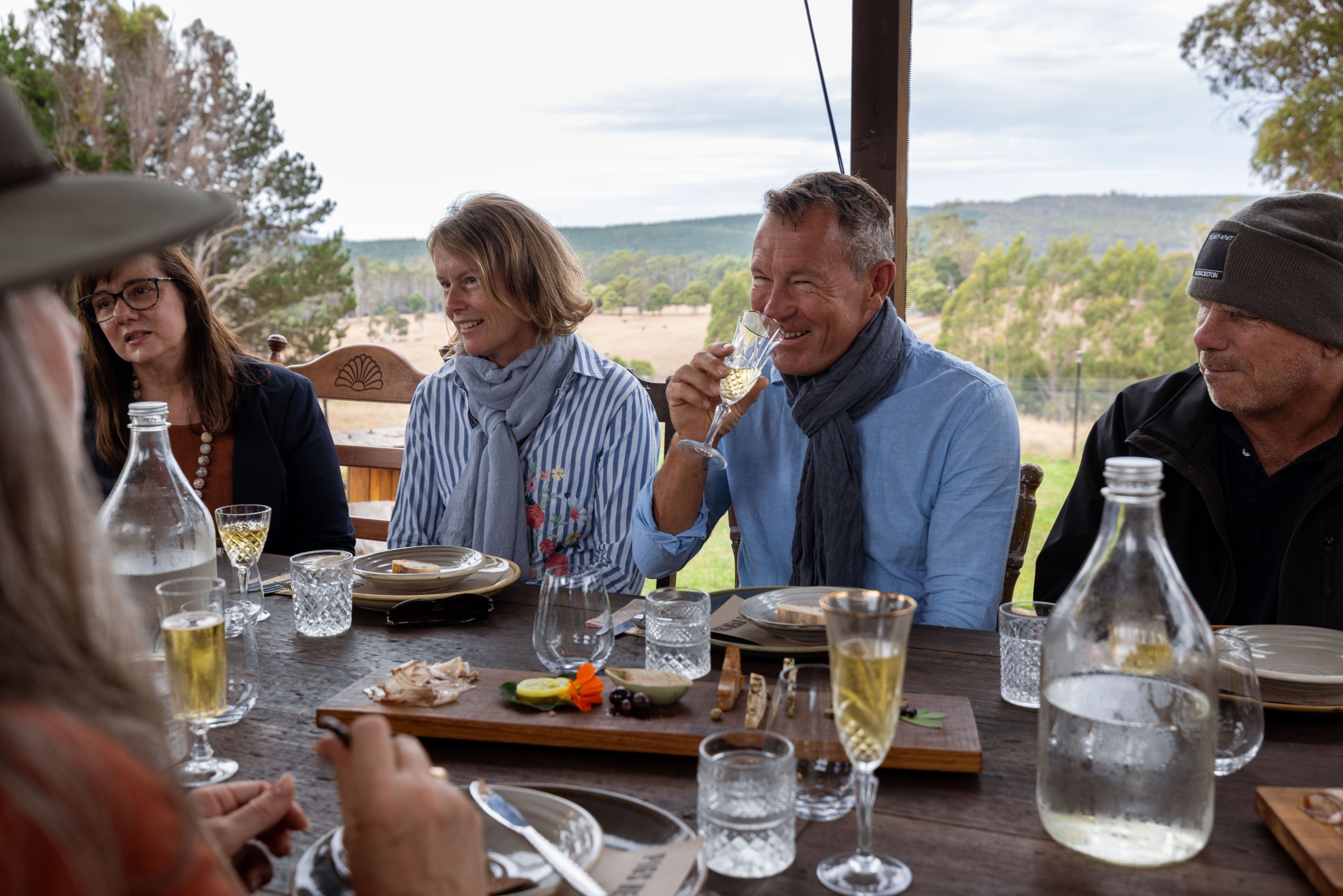 Guests enjoying a long table lunch with shared platters and wine overlooking rolling farmland at Fork it Farm, Lebrina