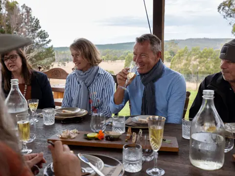 Guests enjoying a long table lunch with shared platters and wine overlooking rolling farmland at Fork it Farm, Lebrina