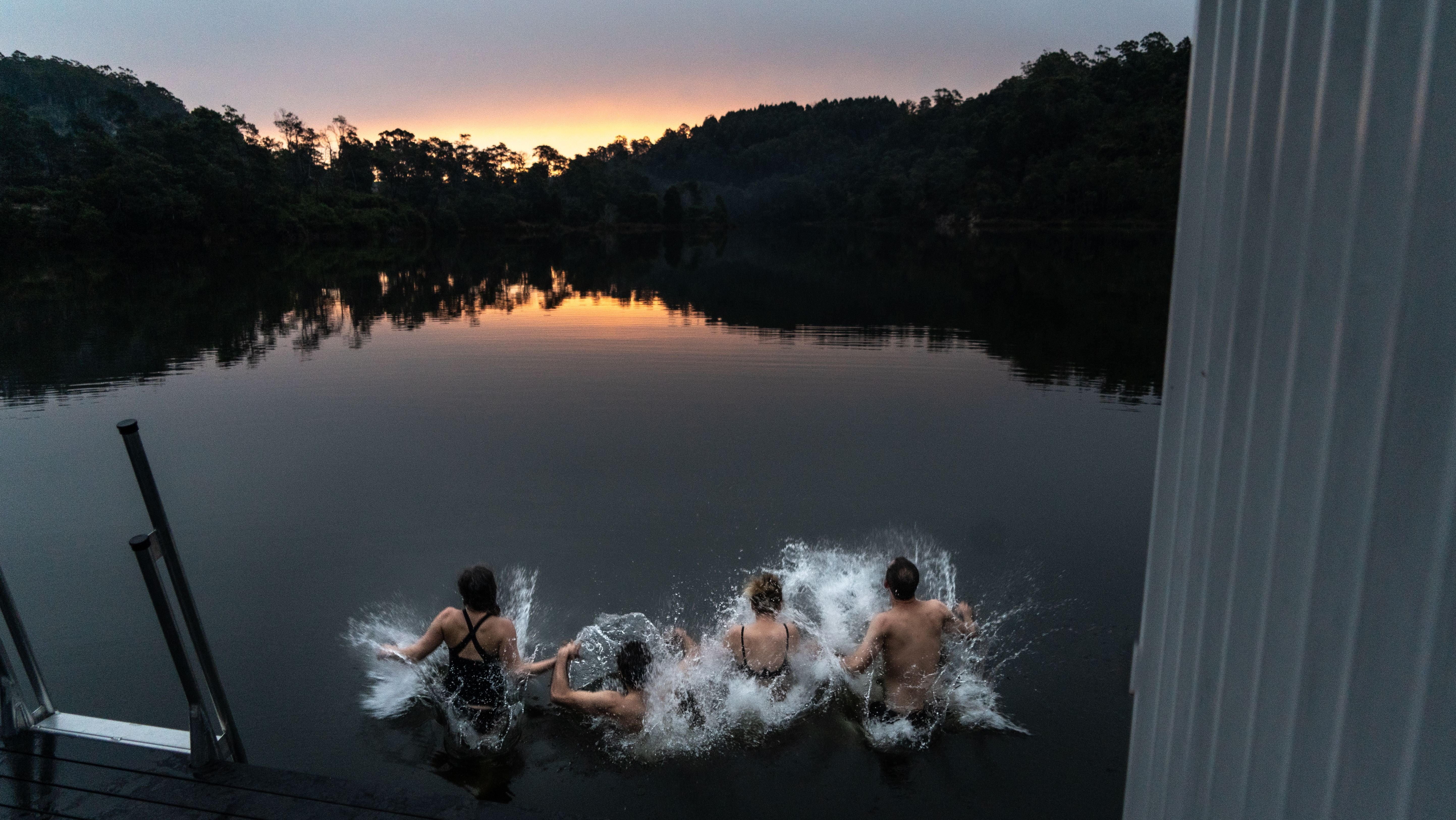 Four bathers leaping into the water from Floating Sauna Lake Derby at twilight, Derby