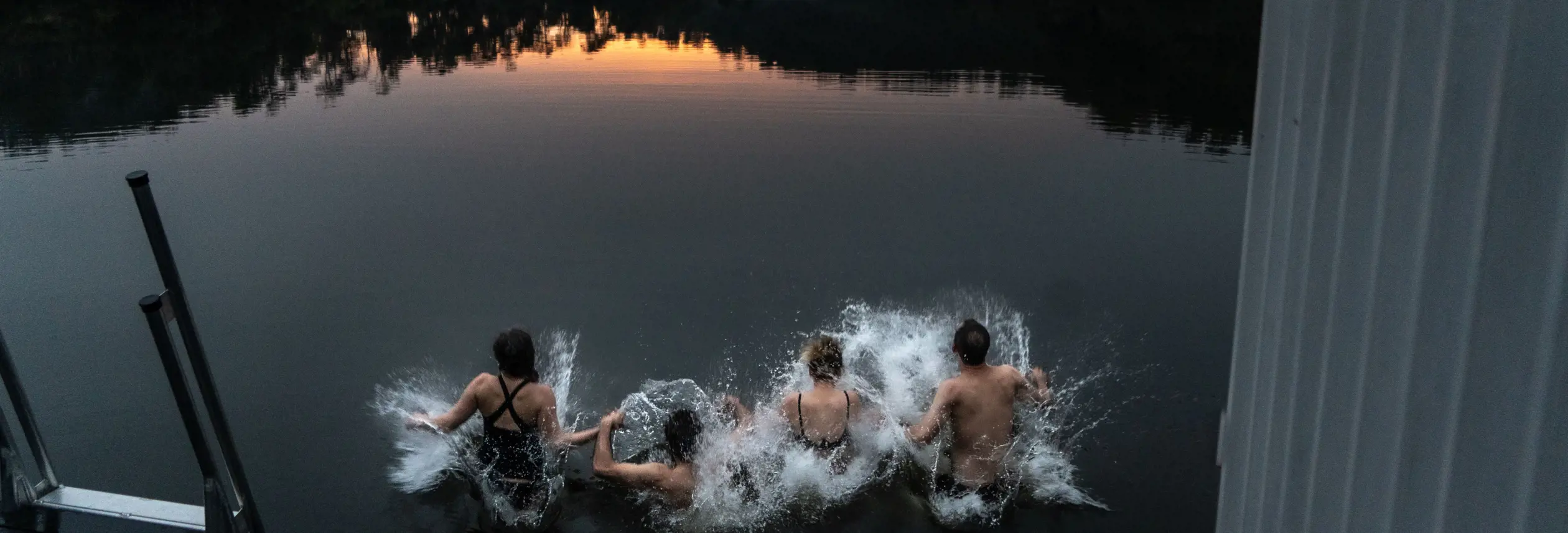 Four bathers leaping into the water from Floating Sauna Lake Derby at twilight, Derby