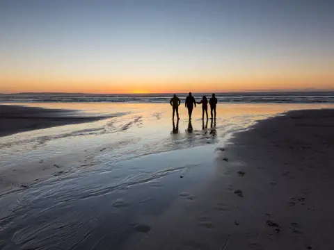 Four people silhouetted on Ocean Beach watching the sun set over the water, Strahan
