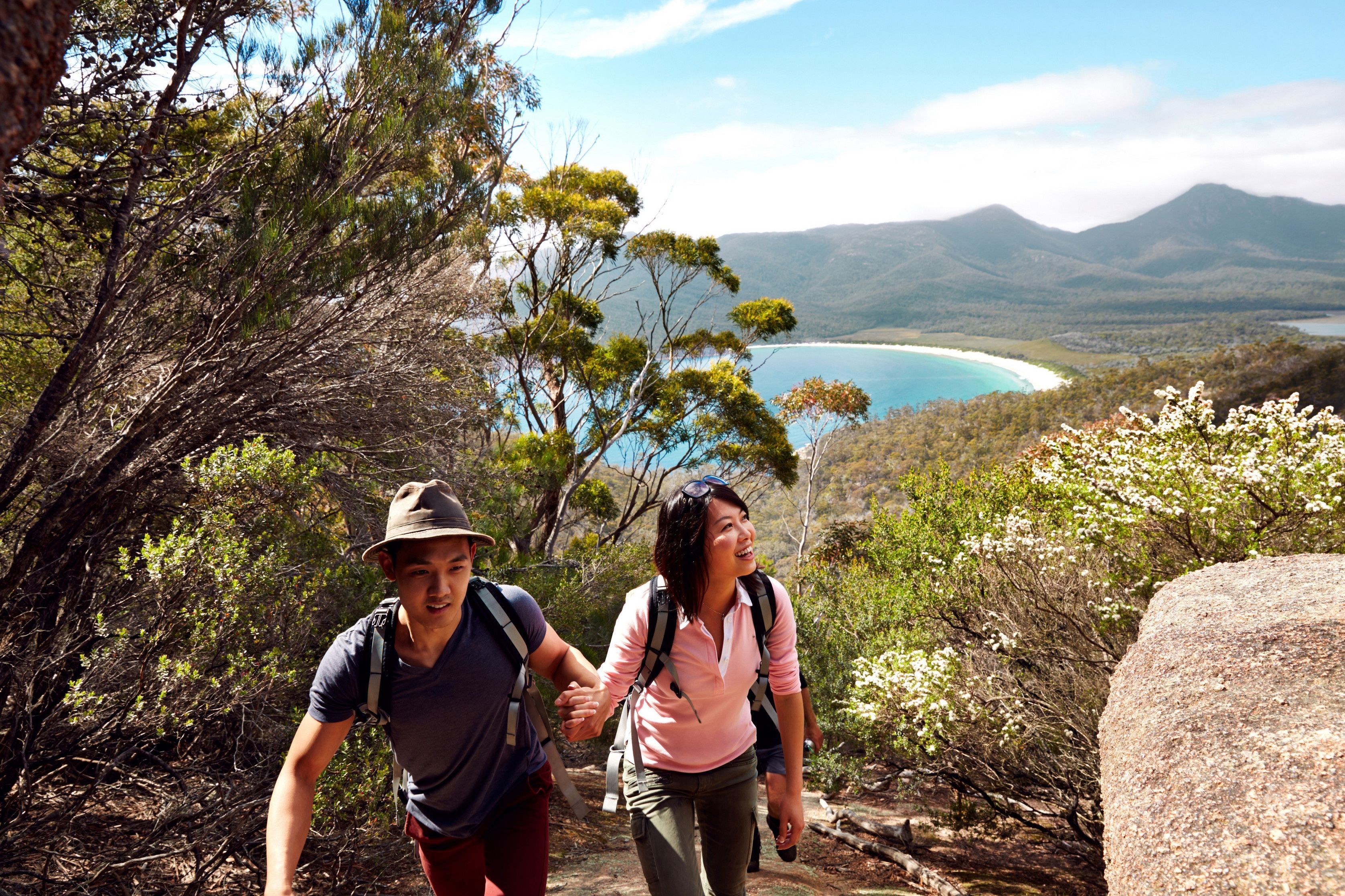 Two walkers ascending the Wineglass Bay Walking Track with the curved beach visible beyond, Freycinet National Park