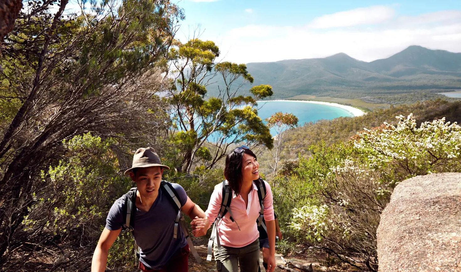 Two walkers ascending the Wineglass Bay Walking Track with the curved beach visible beyond, Freycinet National Park