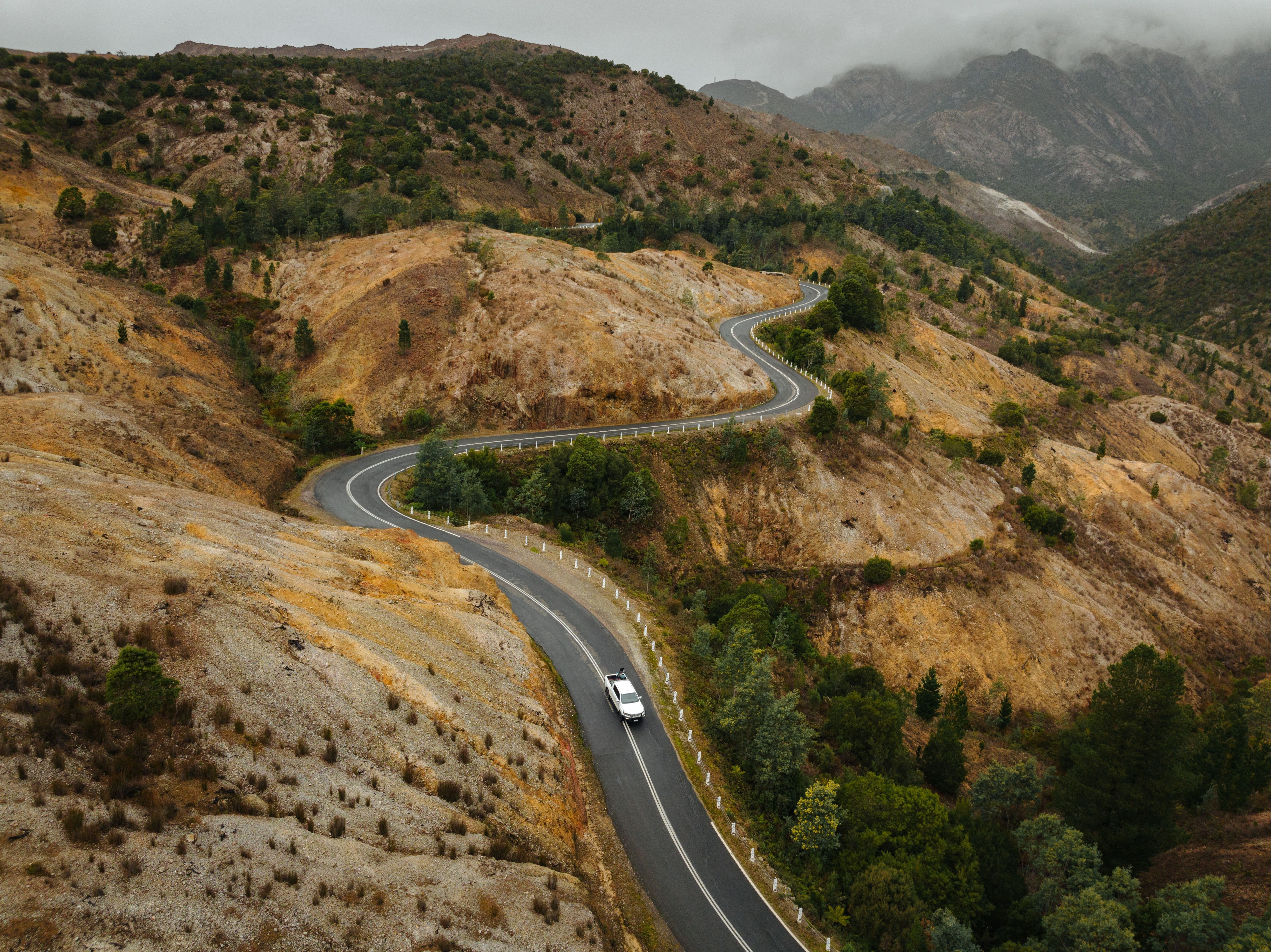 Aerial view of a car winding along the Lyell Highway into Queenstown through the bare conglomerate hillsides, west coast