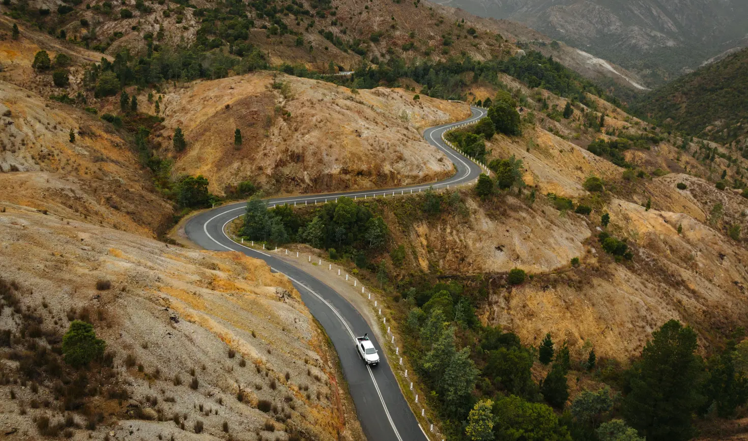 Aerial view of a car winding along the Lyell Highway into Queenstown through the bare conglomerate hillsides, west coast