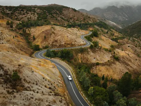 Aerial view of a car winding along the Lyell Highway into Queenstown through the bare conglomerate hillsides, west coast