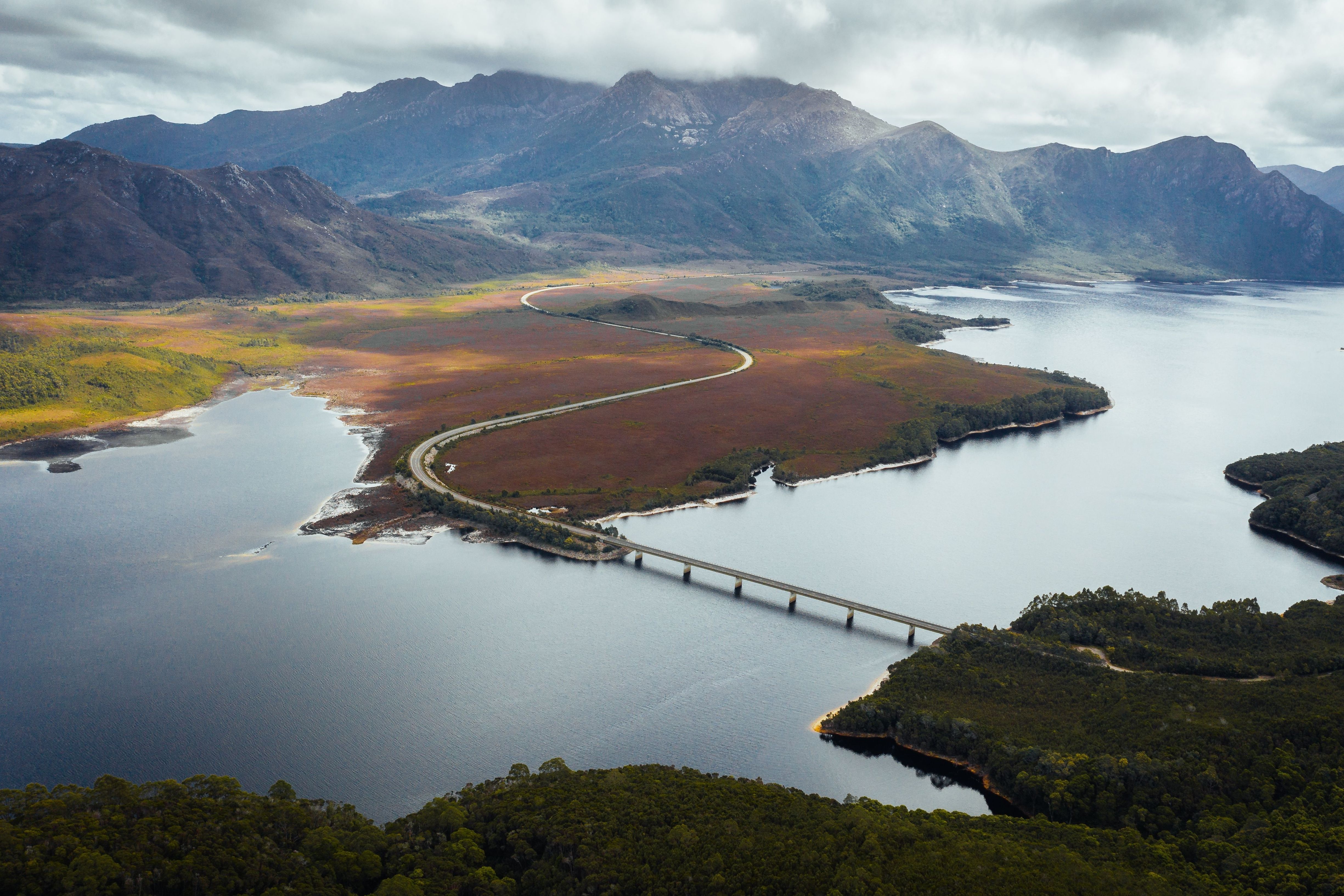 Aerial view of the Lyell Highway crossing the bridge over Lake Burbury with mountain ranges beyond, west coast
