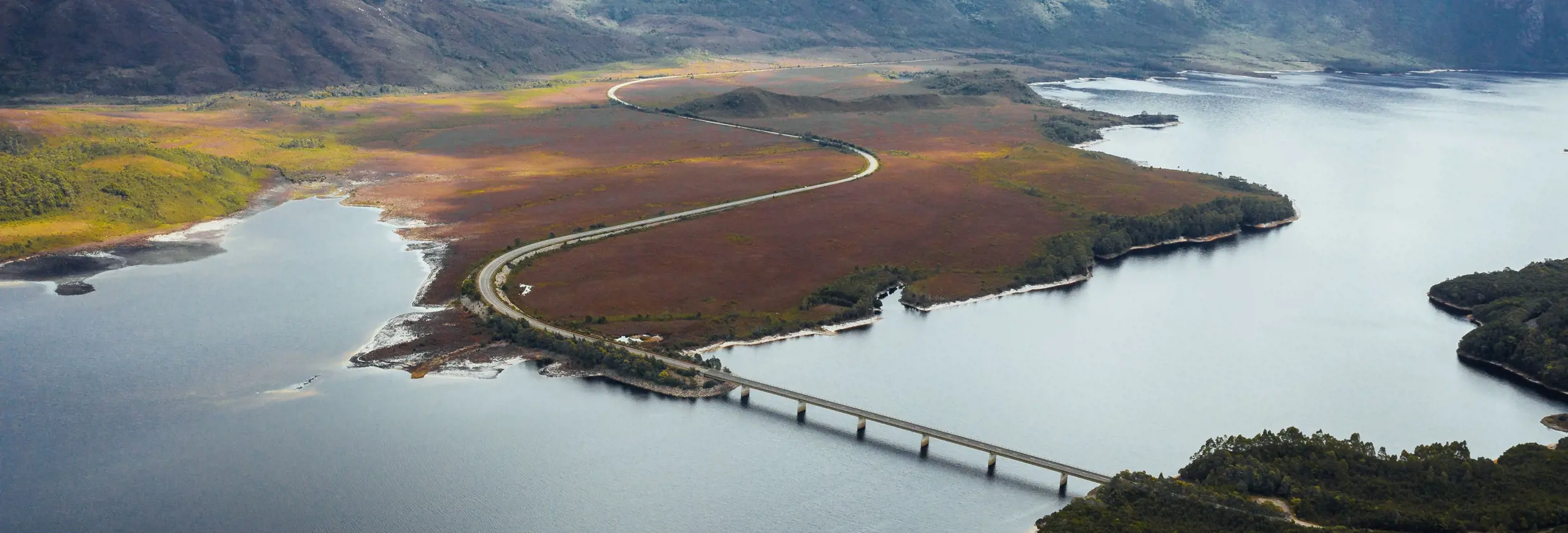 Aerial view of the Lyell Highway crossing the bridge over Lake Burbury with mountain ranges beyond, west coast