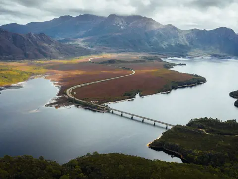 Aerial view of the Lyell Highway crossing the bridge over Lake Burbury with mountain ranges beyond, west coast