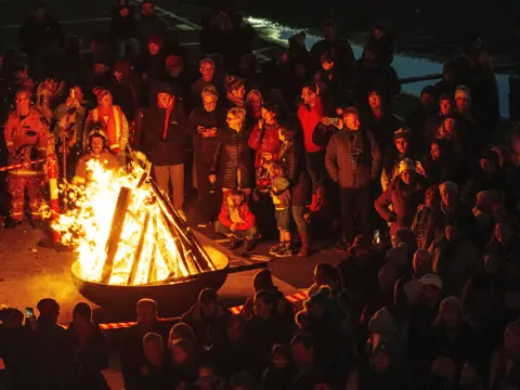 A crowd gathered around a blazing fire pit with fire safety personnel at the Big Sing Bonfire, Festival of Voices, Hobart