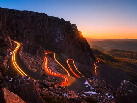 Vehicle light trails curving along the Jacob's Ladder hairpin road at twilight, Ben Lomond National Park