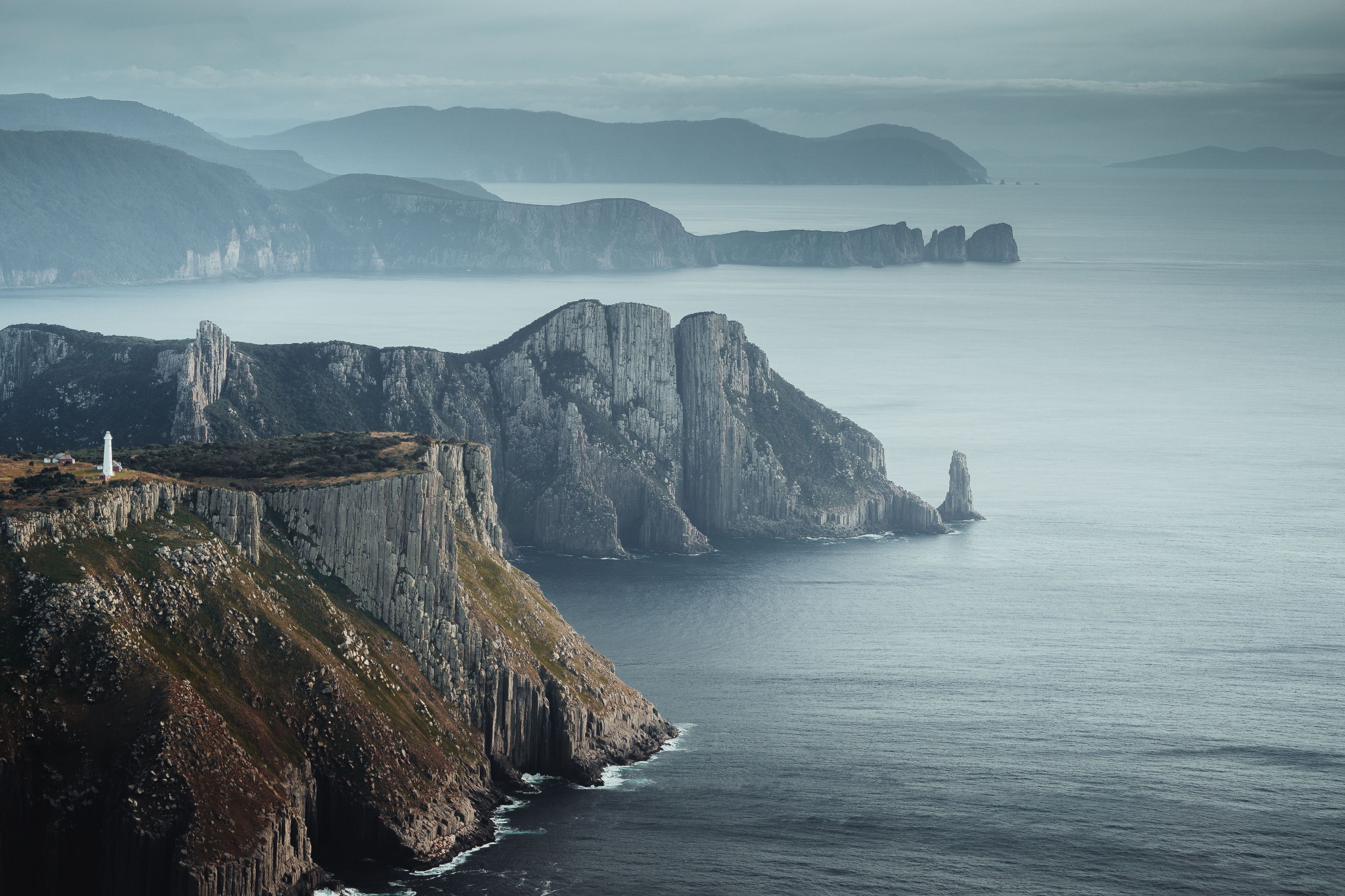 Tasman Island Lighthouse perched on dramatic sea cliffs with misty headlands beyond, Tasman National Park