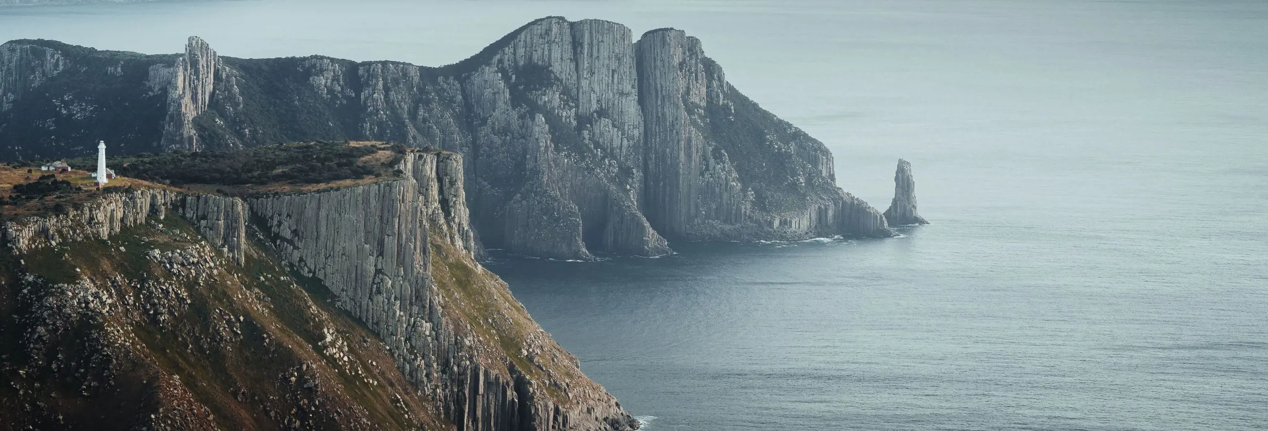 Tasman Island Lighthouse perched on dramatic sea cliffs with misty headlands beyond, Tasman National Park