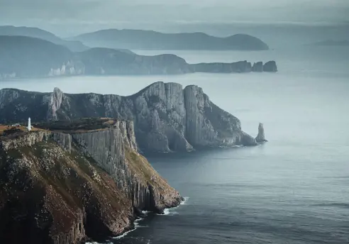 Tasman Island Lighthouse perched on dramatic sea cliffs with misty headlands beyond, Tasman National Park