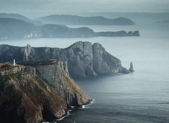 Tasman Island Lighthouse perched on dramatic sea cliffs with misty headlands beyond, Tasman National Park