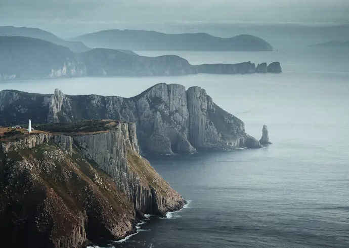 Tasman Island Lighthouse perched on dramatic sea cliffs with misty headlands beyond, Tasman National Park