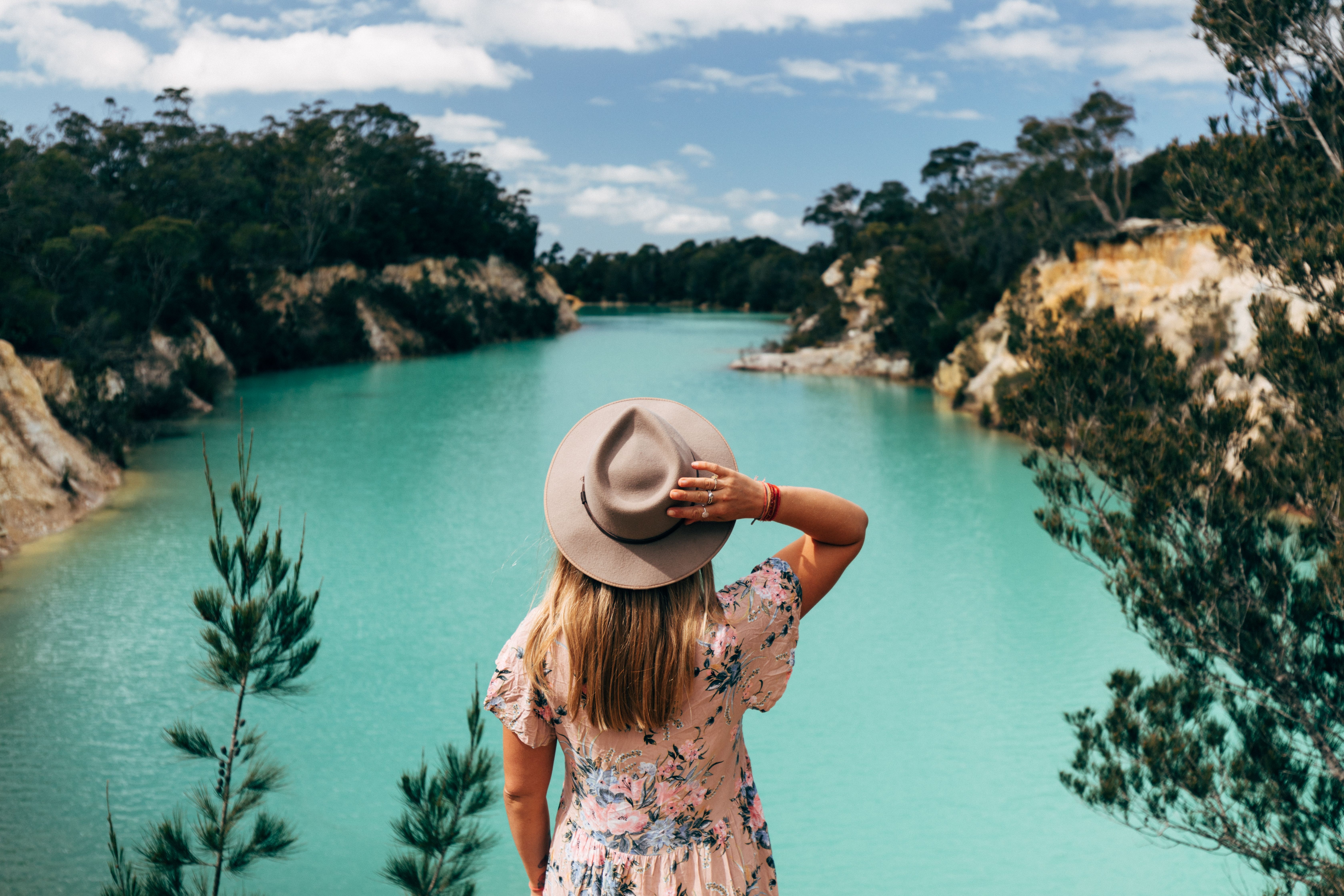A person in a wide brim hat looking out over the turquoise water of Little Blue Lake near Poonerluttener / Mount Cameron